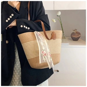Detail of hand-woven straw tote bag featuring brown leather straps and floral lace scarf