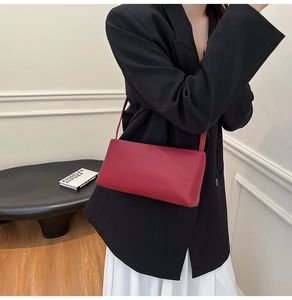 Close-up of minimalist dark burgundy shoulder bag held by a model in a modern urban setting