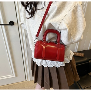 Detail shot of a glossy red patent leather Boston bag with silver hardware and shoulder strap