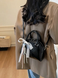 Elegant black glossy leather bowling bag with lace bow accessory shown on shoulder