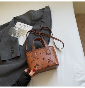 Brown crossbody bucket bag with cartoon prints and adjustable strap on grey blazer