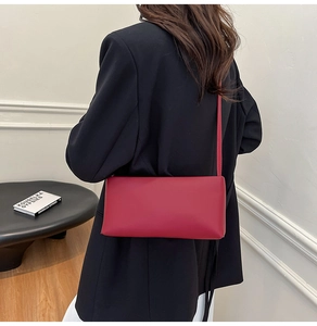 Deep red leather shoulder bag styled on model with minimalist modern interior setting
