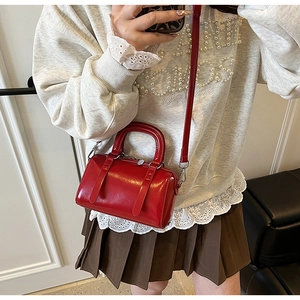 Detail of red mini Boston bag with glossy finish and adjustable crossbody strap