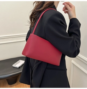 Model wearing a burgundy matte leather shoulder bag in a minimalist style against a white wall