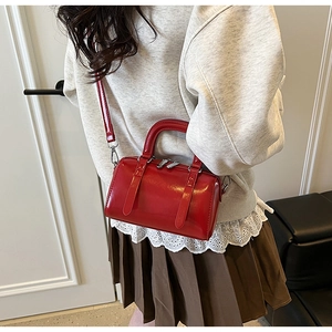 Detail of red glossy mini Boston bag with silver zippers and adjustable crossbody strap