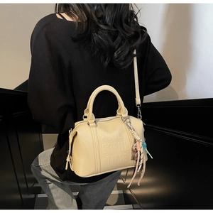 Detail of a beige Boston bag featuring embossed 'CHEERFUL TIME' text and cute bear charm