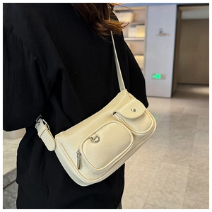 Detail of cream shoulder bag featuring functional front pockets and adjustable strap