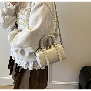 Close-up of cream Boston bag showing glossy patent finish and dual silver-tone zippers
