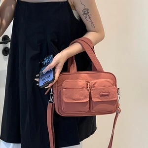 Detail of reddish-brown nylon crossbody bag with dual front zipper pockets and shoulder strap