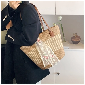 Close-up of straw woven tote bag featuring white lace and floral embroidery details