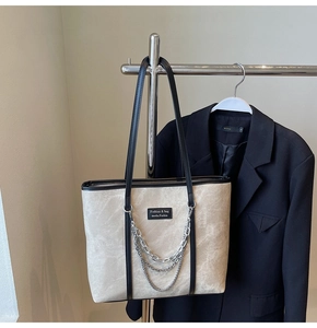 Détail d'un sac cabas beige avec garniture en cuir noir et chaînes argentées
