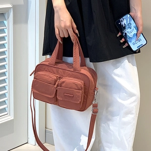 Detail view of brick red utility crossbody bag with functional double front zipper pockets