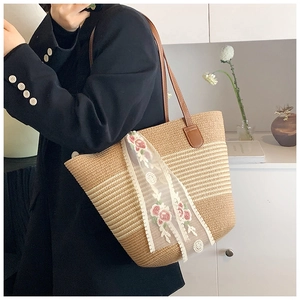 Close-up of woven straw tote bag with floral lace ribbon and brown leather straps