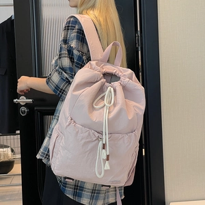 Side view of a casual pink nylon drawstring backpack worn by a model for travel use
