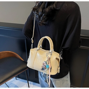 Macro view of cream Boston bag featuring embossed lettering and plush bear charm