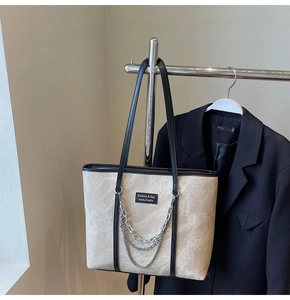 Détail d'un sac cabas beige avec bordure noire et décoration triple chaîne argentée