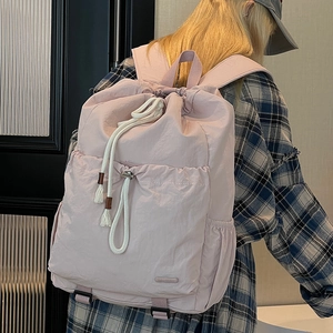 Detail of light pink drawstring nylon backpack featuring side pockets and cord decoration