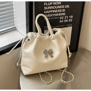 Close-up of cream white chain bag featuring pleated faux leather and silver bow detail