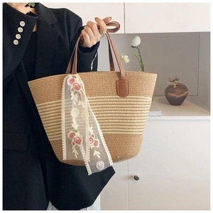 Detail of a woven straw tote bag with brown leather handles and rose embroidery lace scarf