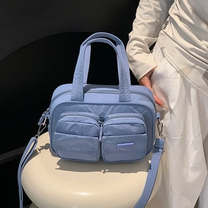 Detailed view of light blue nylon utility handbag with front dual zipper pockets
