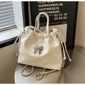 Detail of white leather drawstring bag featuring a silver bow and metal chain strap