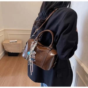 Detail of brown leather Boston bag featuring a logo emboss and cute dog charm on model
