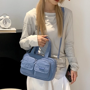 Detail view of light blue utility crossbody bag showing double flap pockets and nylon texture