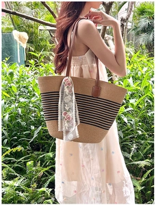 Detail of straw tote bag with black stripes and rose embroidery scarf in a garden