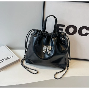 Detail view of black pleated bucket bag with silver bow ornament and chain strap