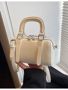 Fashionable cream mini Boston bag with shiny finish and adjustable strap in hand