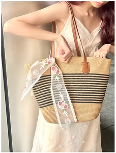 Detail of straw tote bag with black stripes and floral lace ribbon on leather strap
