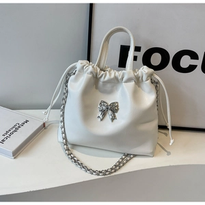 Close-up of a white pleated cloud bag featuring a silver metal bow and woven chain strap