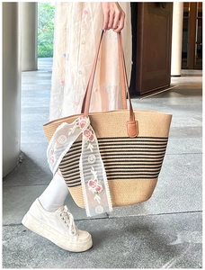 Detail of straw tote bag with black stripes, leather handles and floral lace scarf