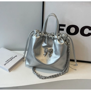 Detail of silver metallic bucket bag with rhinestone bow and drawstring chain strap