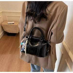 Detail of black glossy Boston bag with embossed logo and a cute decorative bear charm