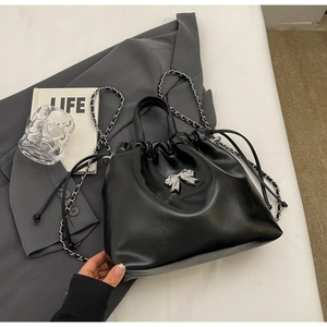 Close-up of black leather bucket bag with silver bow charm on a grey suit background