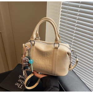 Detail of beige Boston handbag featuring debossed text and cute bear charm accessory