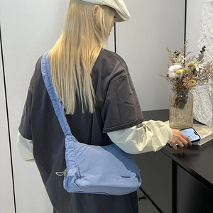 Detailed side view of light blue padded nylon hobo bag with wide strap and drawstring detail