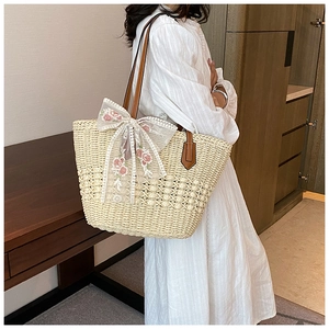 Detail of handwoven straw tote bag with floral lace bow and brown leather strap