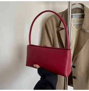 Close-up of wine red leather baguette bag held against a stylish office outfit