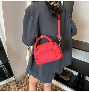 Dettaglio borsa boston in pelle rossa opaca con ciondolo a cuore su sfondo grigio