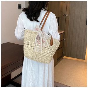 Detail of woven straw tote bag with brown leather straps and white lace floral bow decoration