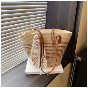 Detail of striped straw tote bag featuring brown leather handles and floral lace scarf