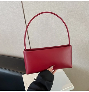 Detail of a dark red leather baguette bag with a slim handle shown in a studio setting