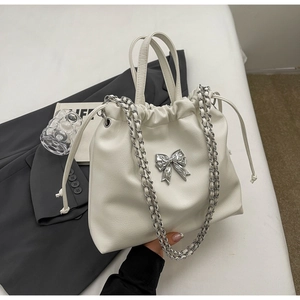 Close-up of white leather pleated bag with silver metal bow and woven chain strap