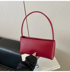 Detailed side view of a minimalist deep red leather handbag with a smooth matte finish