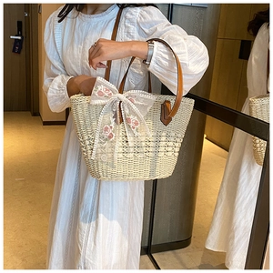 Detail of straw tote bag featuring floral embroidery, lace bow, and leather handle