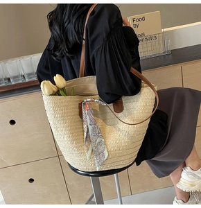 Detail of hand-woven straw tote with brown leather handles and decorative floral scarf