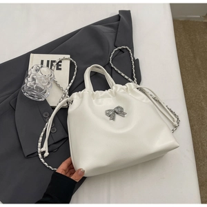 Close-up of cream pleated chain bag featuring silver bow detail and drawstring closure