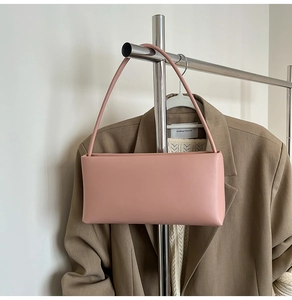 Detail of pink rectangular leather shoulder bag hanging on a rack with a blazer background